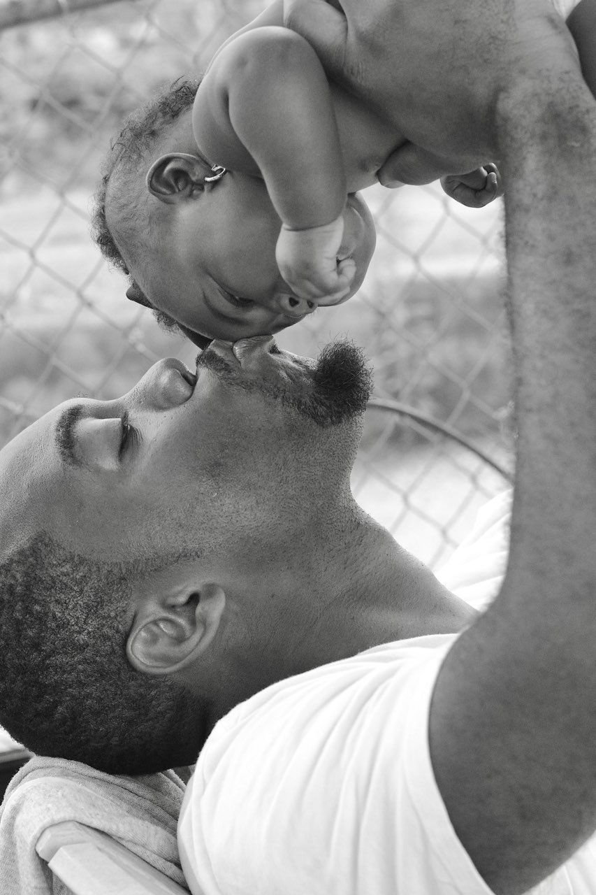 Black and white photograph of a father lifting his baby and kissing the baby’s head